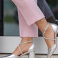 Silver high-heeled shoes worn with light pink pants on a blurred background