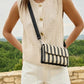 Person wearing a beige sleeveless vest and white shorts, holding a black and white striped bag with a scenic background.