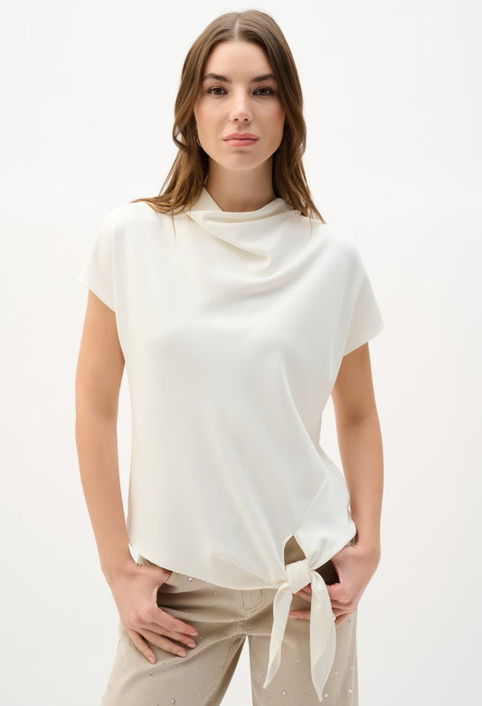 Woman wearing a white cowl-neck top with a tie detail on a white background