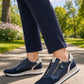 Person wearing navy blue sneakers with white soles on a paved path with greenery in the background