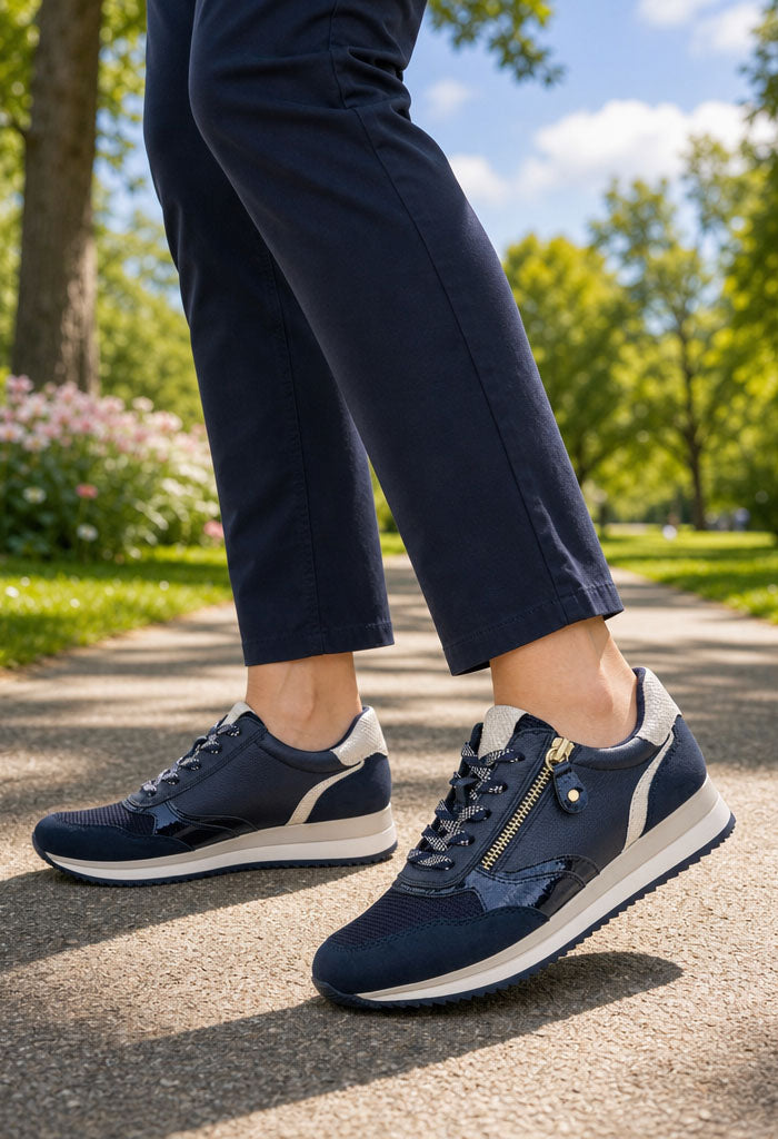 Person wearing navy blue sneakers with white soles on a paved path with greenery in the background