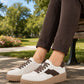 White sneakers with brown accents worn by a person sitting on a park bench.