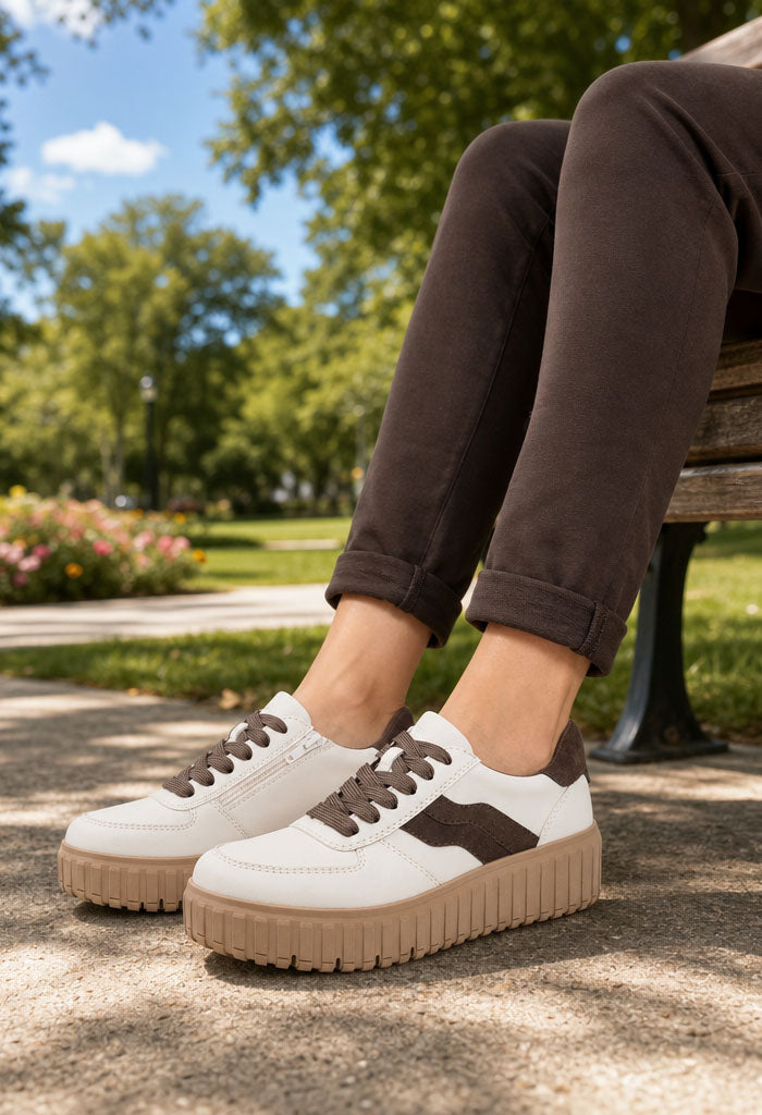 White sneakers with brown accents worn by a person sitting on a park bench.