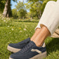 Navy blue sneakers with white soles worn on grass