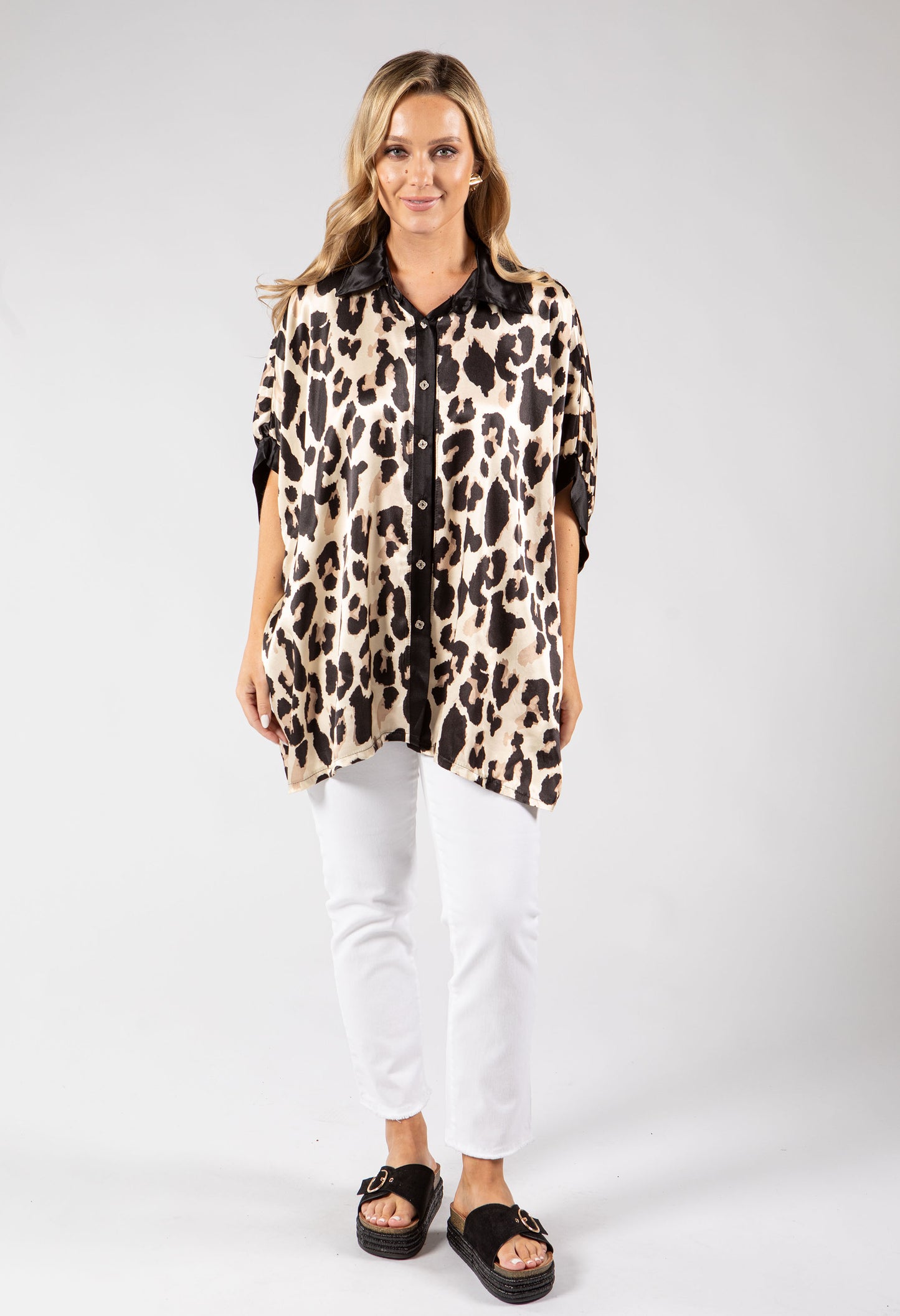 Woman wearing a leopard print shirt and white pants on a gray background
