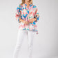 Woman wearing a colorful patterned blouse and white pants on a gray background