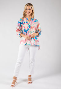 Woman wearing a colorful patterned blouse and white pants on a gray background
