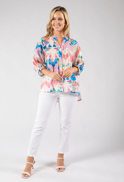 Woman wearing a colorful patterned blouse and white pants on a gray background