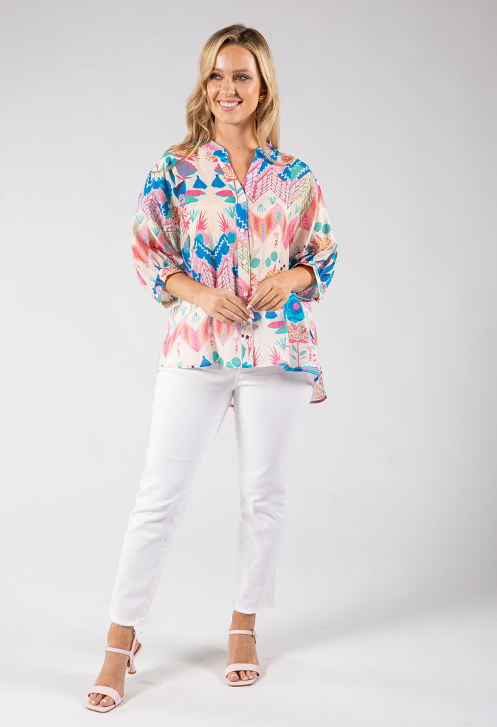 Woman wearing a colorful patterned blouse and white pants on a gray background