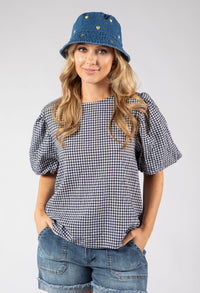 Woman wearing a checkered top, denim shorts, and a denim bucket hat on a white background