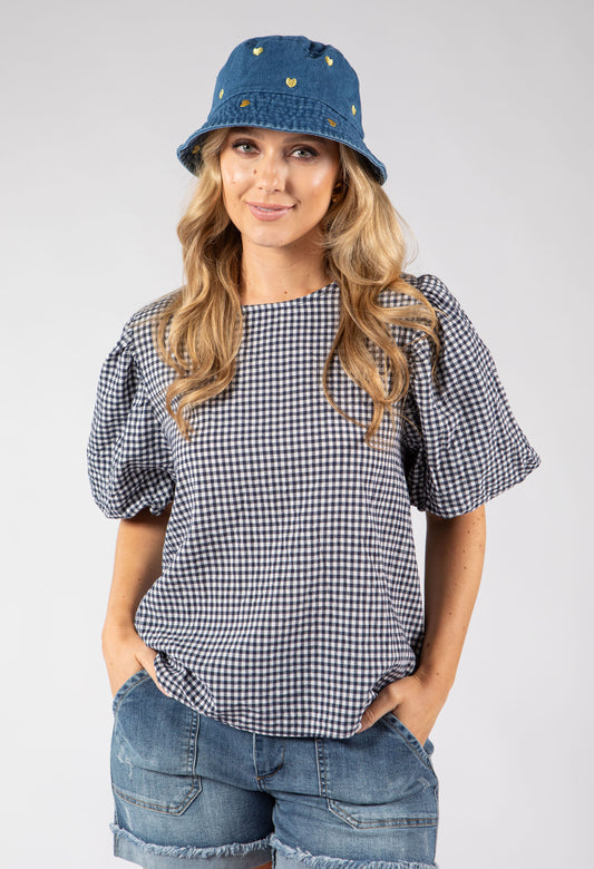 Woman wearing a blue denim bucket hat with gold buttons on a gray background