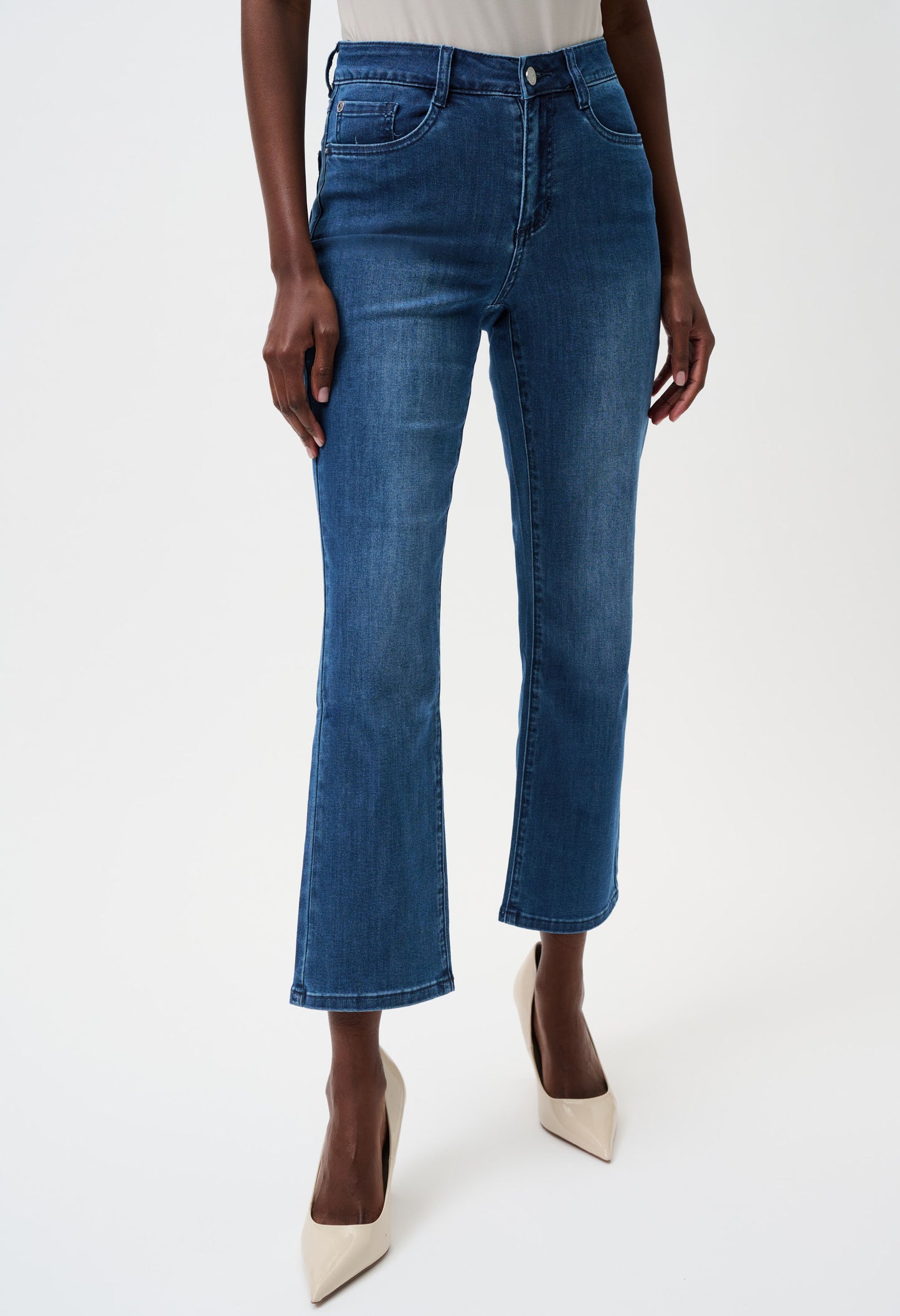A model wearing a pair of medium-wash blue denim flare jeans with a cropped ankle length, paired with beige pointed-toe heels against a plain white studio background.