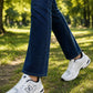 White  sneakers worn with dark blue jeans, shown on a person walking on a grassy park path.