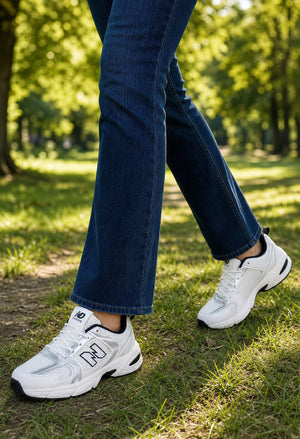 White  sneakers worn with dark blue jeans, shown on a person walking on a grassy park path.