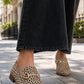 A person wearing black wide-leg jeans and leopard-print loafers with gold horsebit details, standing on a paved outdoor walkway.