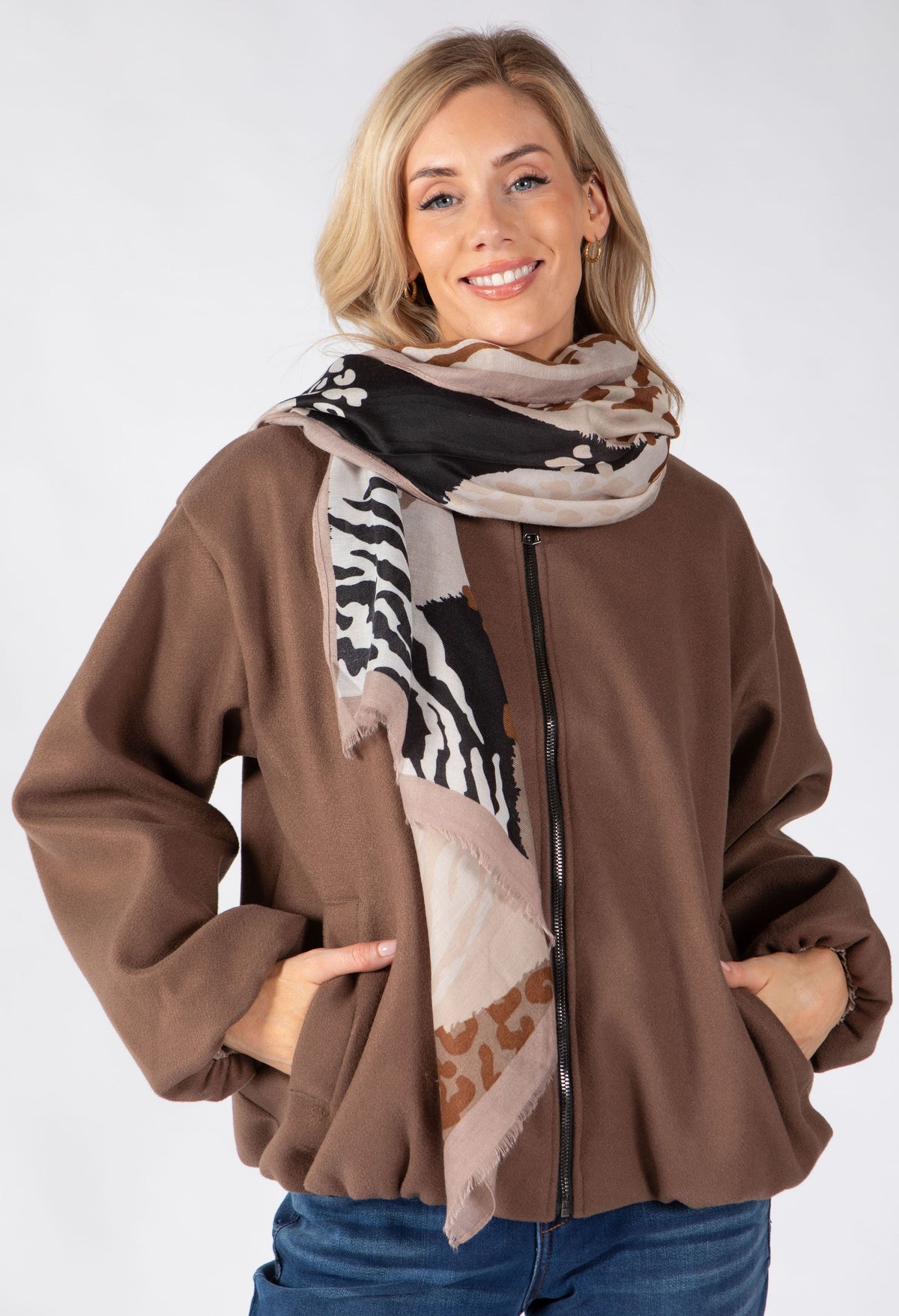 A woman wearing a brown zip-up jacket and a patterned scarf with zebra and leopard print details, posed against a light gray studio background.