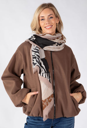 A woman wearing a brown zip-up jacket and a patterned scarf with zebra and leopard print details, posed against a light gray studio background.