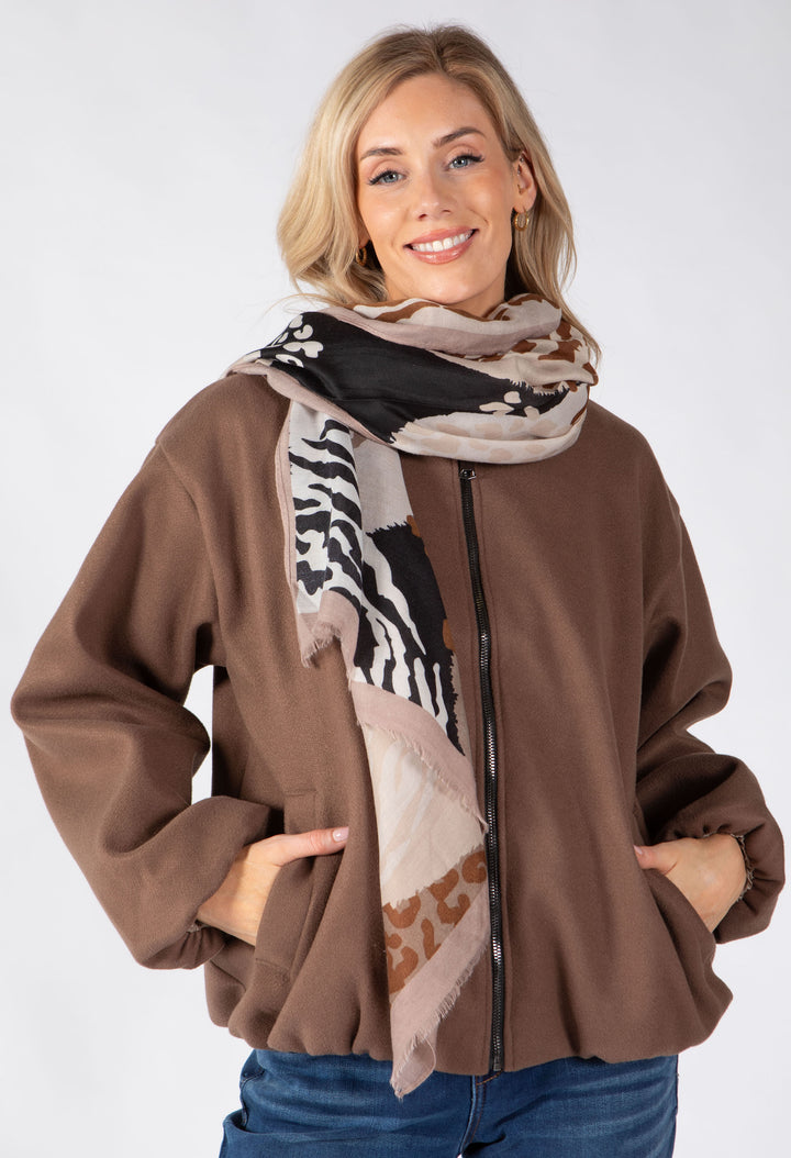 A woman wearing a brown zip-up jacket and a patterned scarf with zebra and leopard print details, posed against a light gray studio background.